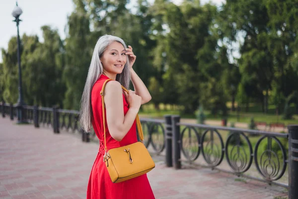 Profile side photo of mature attractive asian woman happy positive smile hold bag walk city center outdoors