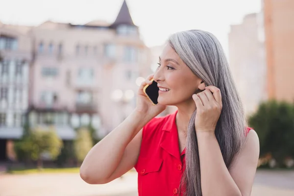 Portrait of attractive cheerful grey-haired woman talking on cell traveling abroad downtown center outdoors — Stockfoto