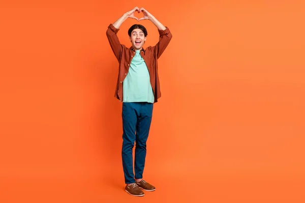 Full size photo of cheerful positive handsome male show heart sign above head isolated on orange color background — Stockfoto