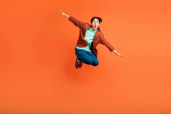 Full size photo of smiling guy jumping fooling around hands wings plane fly isolated on orange color background — Stock Fotó