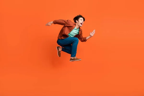 Foto lateral de perfil de tamaño completo del hombre funky feliz corriendo en el espacio de copia de aspecto de aire que viaja aislado sobre fondo de color naranja —  Fotos de Stock