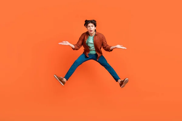 Full size photo of unhappy upset man jumping shrug shoulders wtf hesitant doubt isolated on orange color background — Stockfoto