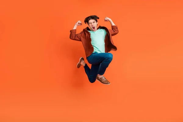 Foto in voller Größe von glücklich aufgeregt funky lustige Kerl springen zeigt Muskeln Sieg isoliert auf orangefarbenem Hintergrund — Stockfoto