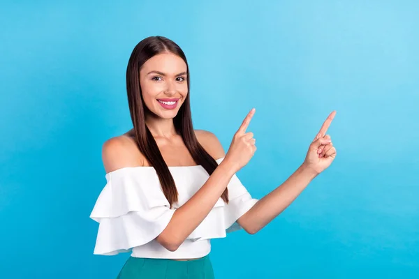 Photo of positive cheerful lady two fingers indicate empty space wear white blouse isolated blue color background — стоковое фото
