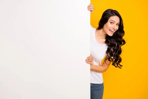 Portrait of lovely curious glad cheerful wavy-haired girl holding big board copy space ad isolated over bright yellow color background — kuvapankkivalokuva
