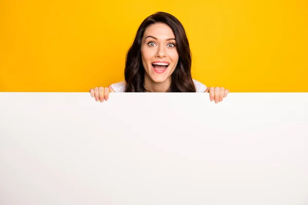 Photo of impressed funny young lady dressed white t-shirt holding white bill board empty space isolated yellow color background — kuvapankkivalokuva