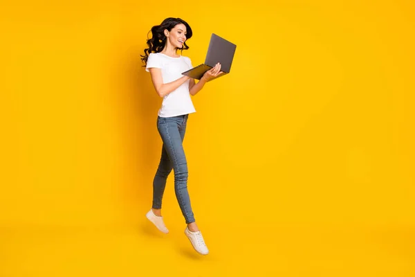 Photo of adorable sweet young woman wear white t-shirt jumping holding modern device empty space isolated yellow color background — Foto Stock