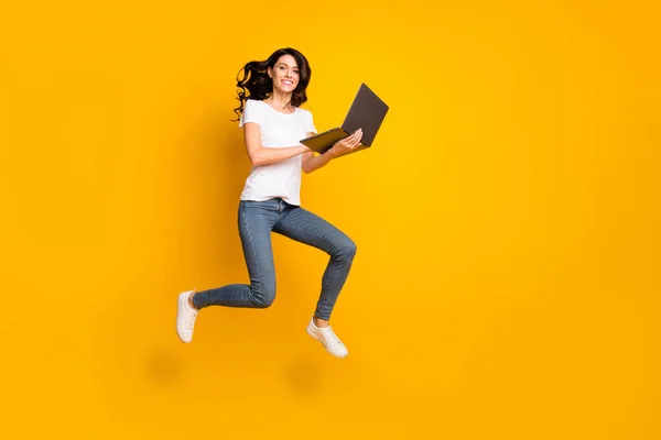Vista completa del tamaño del cuerpo de la encantadora chica alegre saltando utilizando el éxito del ordenador portátil aislado sobre el fondo de color amarillo brillante —  Fotos de Stock