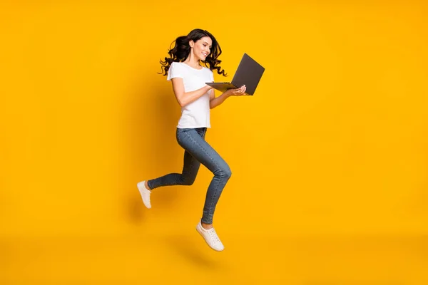 Photo of cute pretty young lady dressed white t-shirt jumping high typing modern gadget isolated yellow color background — Φωτογραφία Αρχείου