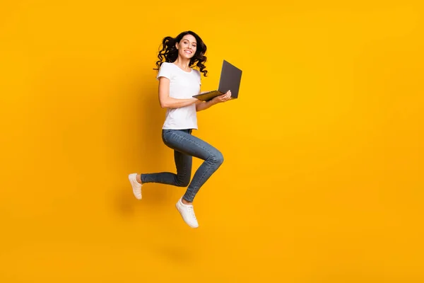 Photo of sweet shiny young woman wear white t-shirt jumping holding modern device isolated yellow color background — Φωτογραφία Αρχείου