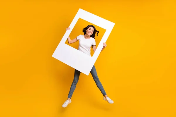 Full length body size view of lovely cheerful girl jumping having fun holding photo frame isolated over bright yellow color background — Foto Stock