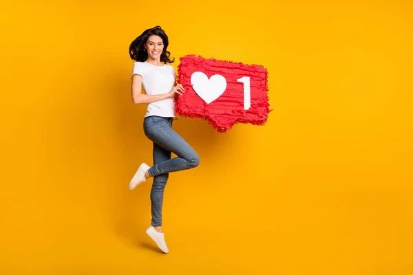 Full length body size view of pretty cheerful girl jumping holding red like board chat isolated over bright yellow color background — Fotografia de Stock