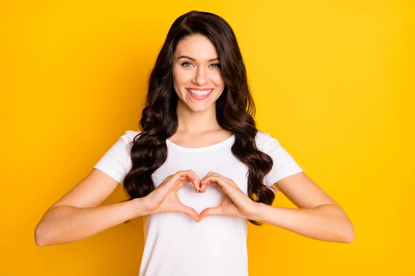 Foto de menina bonita doce vestida t-shirt branca mostrando dedos coração isolado cor amarela fundo — Fotografia de Stock