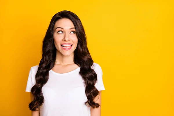 Foto de linda mujer joven astuta usar camiseta blanca que muestra la lengua buscando espacio vacío aislado color amarillo fondo — Foto de Stock