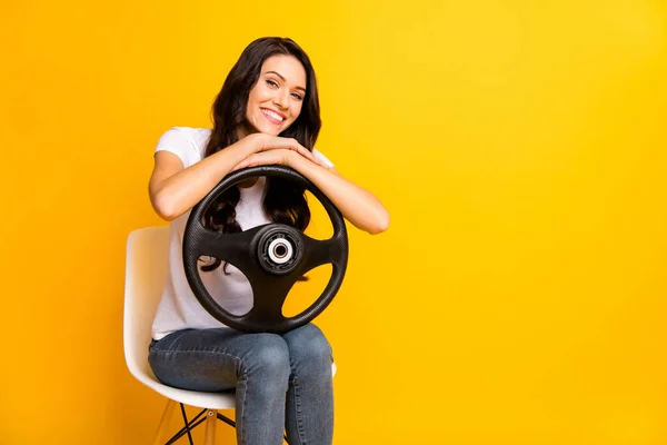 Portrait of lovely cheerful wavy-haired girl holding steering wheel sitting in chair isolated over bright yellow color background — Stok fotoğraf