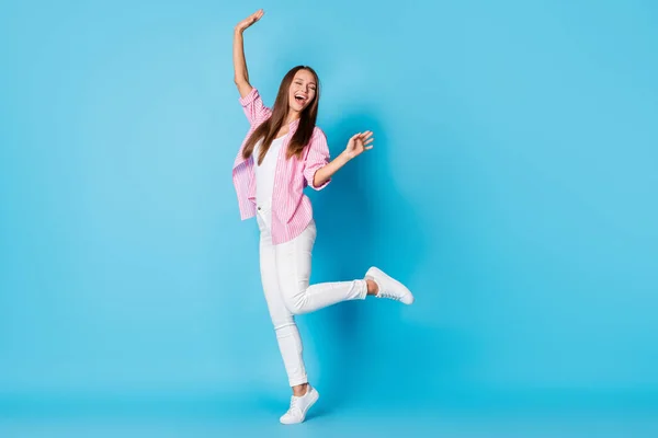 Photo of dreamy inspired lady dance open mouth raise arm wear pink striped shirt trousers footwear isolated blue background — Stockfoto