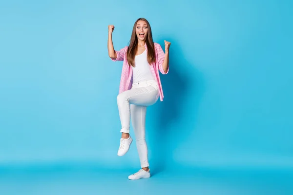 Photo of excited cheerful lady raise fists open mouth wear pink striped shirt pants footwear isolated blue background — Photo