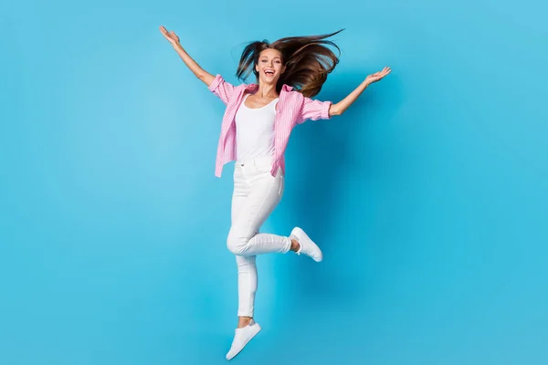 Photo of lady jump raise hands have fun throw hair wear pink striped shirt pants sneakers isolated blue background — Stock Fotó