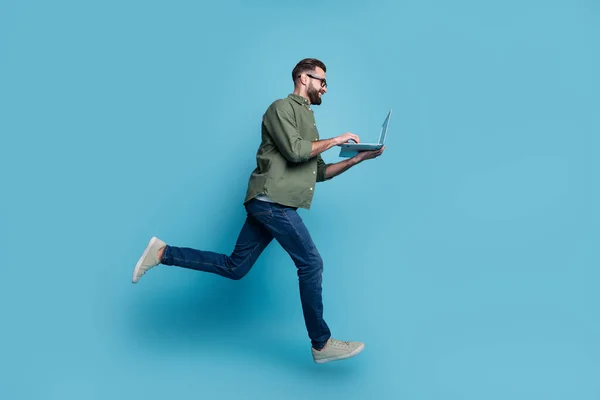 Profile photo of nice freelancer guy jump hold netbook typing email wear specs green shirt isolated blue color background — Zdjęcie stockowe