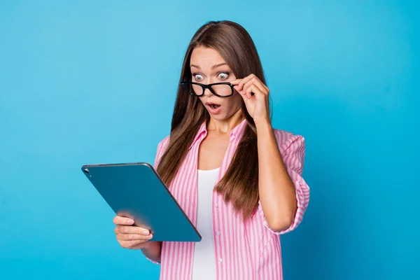 Photo of surprised lady hold tablet look screen open mouth wear specs pink striped shirt isolated blue background — Photo