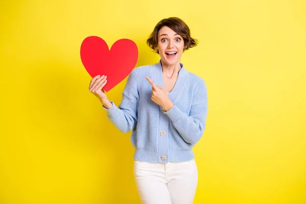Portrait of attractive cheerful amazed girl demonstrating paper heart amour isolated over bright yellow color background — Stockfoto