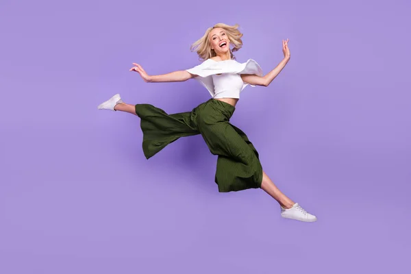 Full length body size photo blonde girl laughing jumping up doing stretching isolated pastel purple color background — стоковое фото