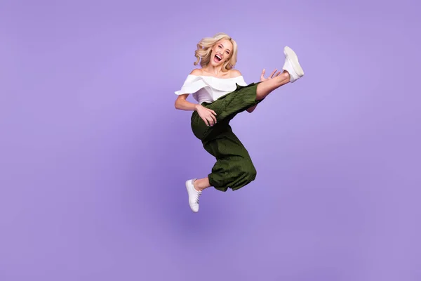 Photo of positive crazy active lady jump raise leg wear white blouse flared trousers isolated violet color background — Stok fotoğraf