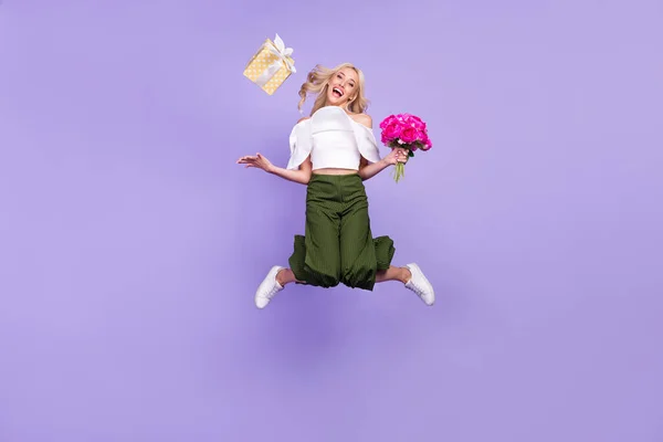 Повна довжина тіла дівчина стрибає вгору, кидаючи подарункову коробку отримала букет квітів ізольований пастельно-фіолетовий кольоровий фон — стокове фото