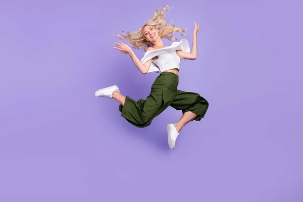 Photo of energetic lady jump relax throw hair wear white blouse flared trousers isolated purple color background