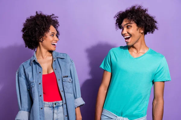 Foto de pareja de piel oscura joven emocionada asombrada se miran noticias frescas aisladas en el fondo de color violeta —  Fotos de Stock