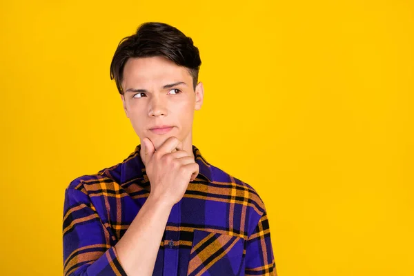 Photo of unsure brunet young guy look empty space wear plaid shirt isolated on yellow color background — Stock Photo, Image