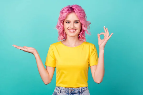 Foto de millennial dulce rosa peinado lady hold espacio vacío mostrar okey desgaste amarillo camiseta aislada sobre fondo verde azulado — Foto de Stock