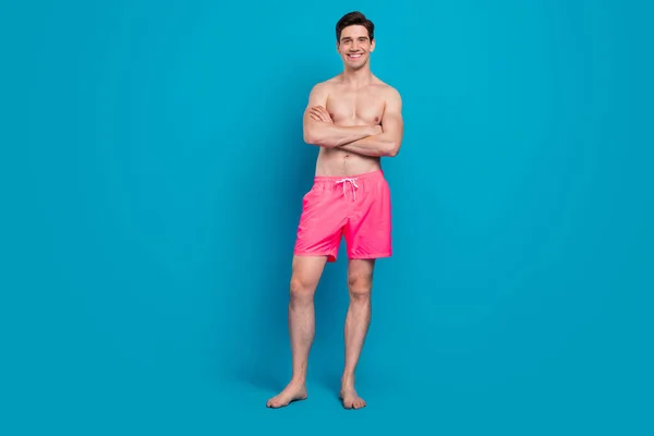 Fénykép magabiztos kedves fickó hajtogatott karok fényes mosoly mezítláb viselni fürdőruha rövidnadrág elszigetelt kék szín háttér — Stock Fotó