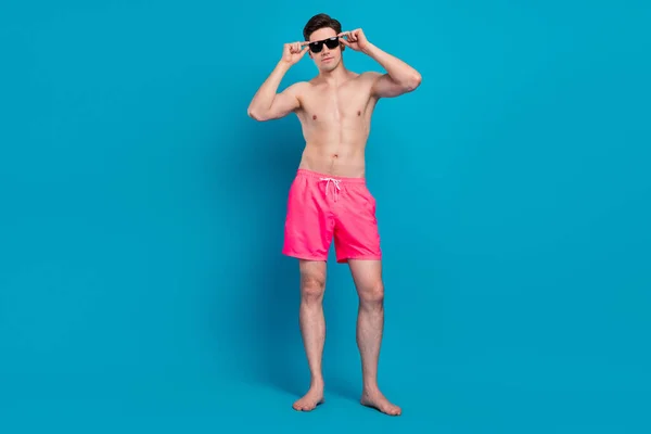 Foto von coolen selbstbewussten Mann posiert barfuß tragen Sonnenbrille Badebekleidung Shorts isoliert blaue Farbe Hintergrund — Stockfoto