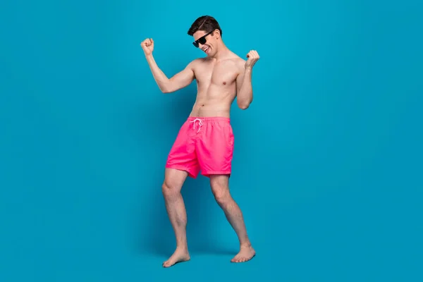 Foto von verrückten unbeschwerten Kerl tanzen clubbing feiern Sieg tragen Sonnenbrille Badebekleidung Shorts isoliert blaue Farbe Hintergrund — Stockfoto