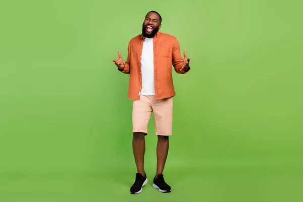Full body foto van optimistische millennial brunet guy zingen dragen shirt shorts schoenen geïsoleerd op groene achtergrond — Stockfoto
