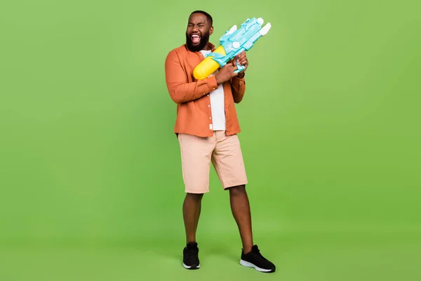 Foto de tamaño completo de fresco joven morena chico mantenga pistola de agua usar camisa pantalones cortos zapatos aislados sobre fondo verde — Foto de Stock