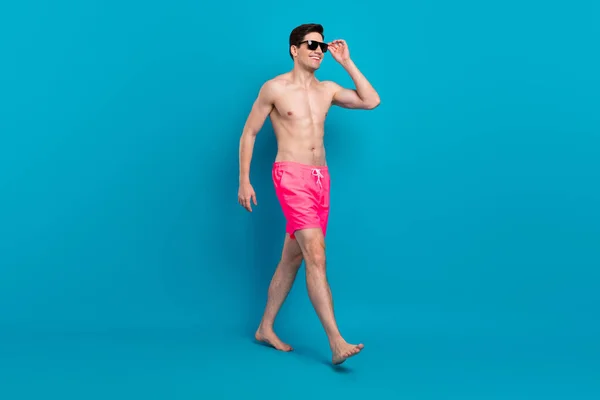 Ganzkörperprofil Seite Foto von jungen Mann glücklich positives Lächeln gehen Schritt tragen Sonnenbrille Urlaub isoliert über blauer Farbe Hintergrund — Stockfoto