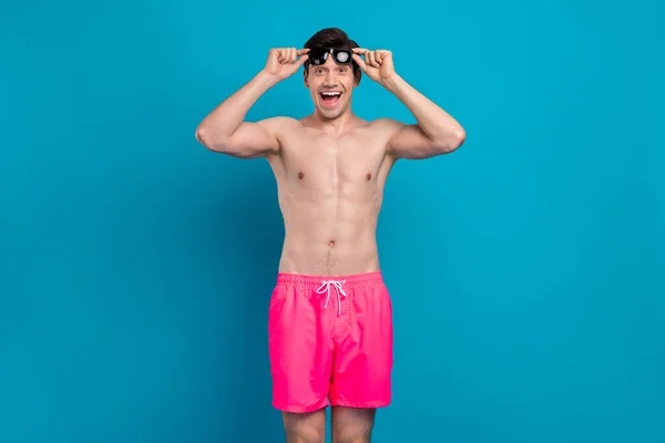 Foto de chico asombrado excitado boca abierta omg reacción desgaste sunglass traje de baño pantalones cortos aislados de color azul fondo — Foto de Stock