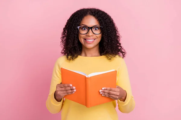 Foto von glänzend beeindruckt dunkelhäutige Frau tragen gelben Pullover Brille hält Werbebuch isoliert rosa Farbe Hintergrund — Stockfoto