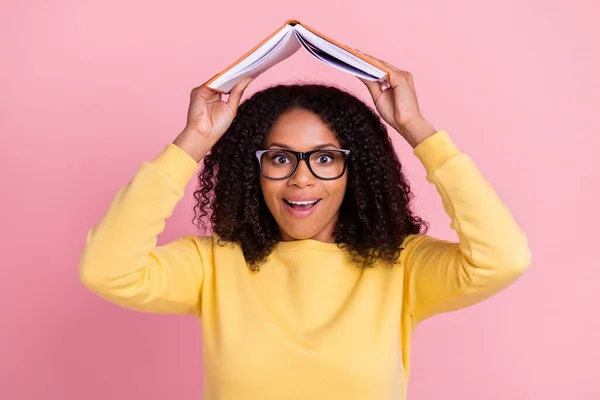 Foto di scioccato divertente scuro ragazza pelle vestito giallo pullover occhiali tenendo libro tetto sorridente isolato colore rosa sfondo — Foto Stock