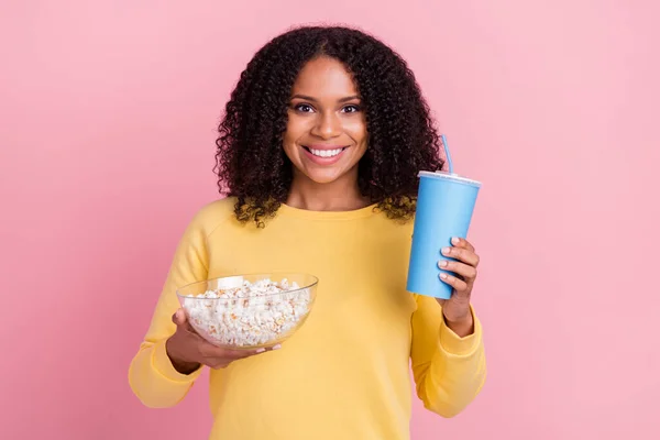 Bild av charmiga söt mörk hud flicka klädd gul pullover innehav läsk popcorn platta ler isolerad rosa färg bakgrund — Stockfoto