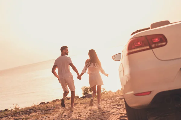 Foto di allegra coppia di sposi spensierati vestiti bianchi guida auto a piedi spiaggia tenendo le braccia all'aperto strada di campagna — Foto Stock