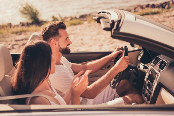 Фото довольно милой супружеской пары, одетой в белую одежду за рулем автомобиля, говорящей улыбаясь на улице — стоковое фото