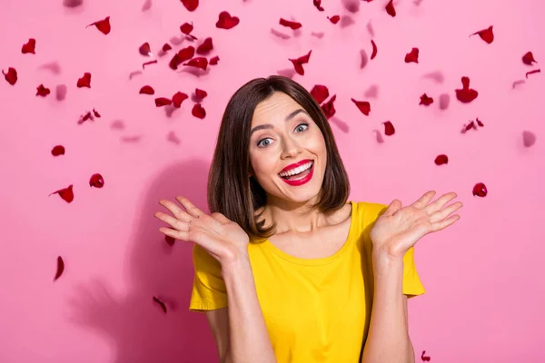 Foto van grappige opgewonden jonge dame gekleed gele kleren glimlachend rijzende armen rode bloemblaadjes vliegen geïsoleerde roze kleur achtergrond — Stockfoto