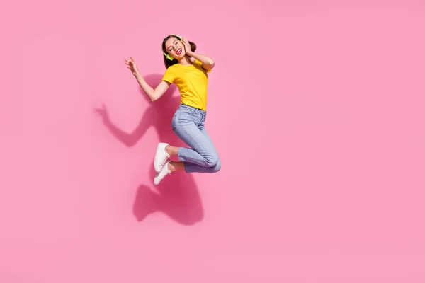 Photo of sweet dreamy young woman wear yellow outfit jumping high listening songs headphones empty space isolated pink color background — Stock Photo, Image