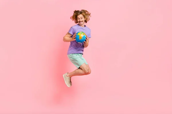 Full length body size view of attractive cheerful guy jumping holding in hands map globe isolated over pink pastel color background — Stock Photo, Image