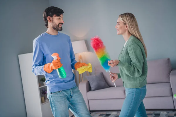 Photo of positive cheerful spouses guy lady clean apartment room hold detergent fluffy duster rag communicating — Stock Photo, Image