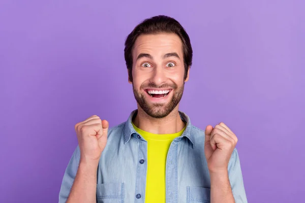 Портрет улыбающегося взволнованного изумленного парня поднимает кулаки в триумфальном достижении победы, изолированном на фиолетовом фоне — стоковое фото
