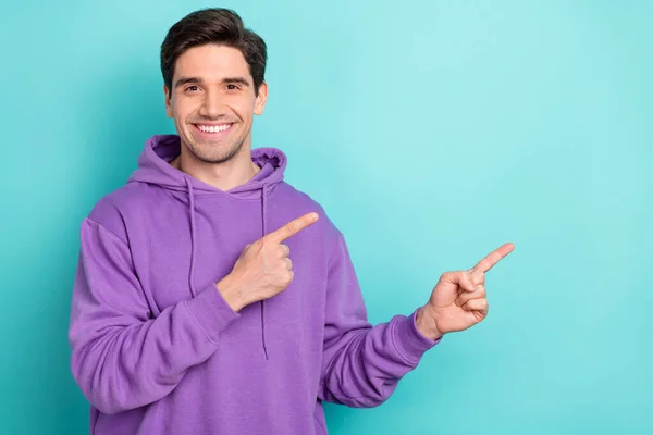 Фотографія впевненого чарівного молодого чоловіка, одягненого в фіолетовий светр посміхаючись, вказуючи на два пальці порожній простір ізольованого кольорового фону — стокове фото